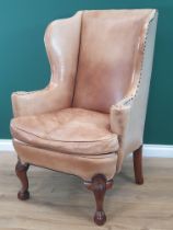 A George III style walnut Wingback Armchair in pale tan leather with outswept arms, raised on carved