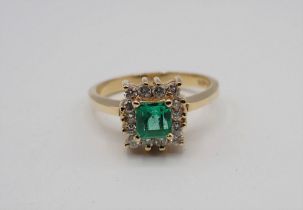 An Emerald and Diamond Cluster Ring corner claw-set step-cut emerald within a frame of fourteen