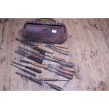 A vintage leather bag full of assorted antique woodworking chisels