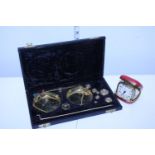 A vintage travel alarm clock and a cased set of brass weighing scales
