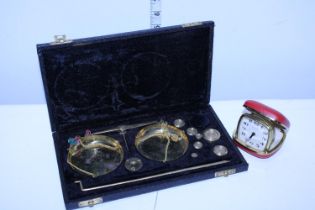 A vintage travel alarm clock and a cased set of brass weighing scales