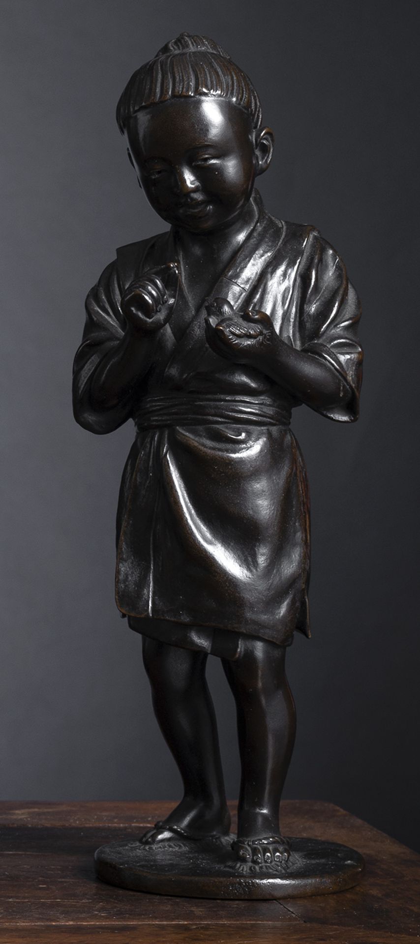 A GOOD BRONZE MODEL OF A STANDING BOY FEEDING A CHICK IN HIS LEFT HAND