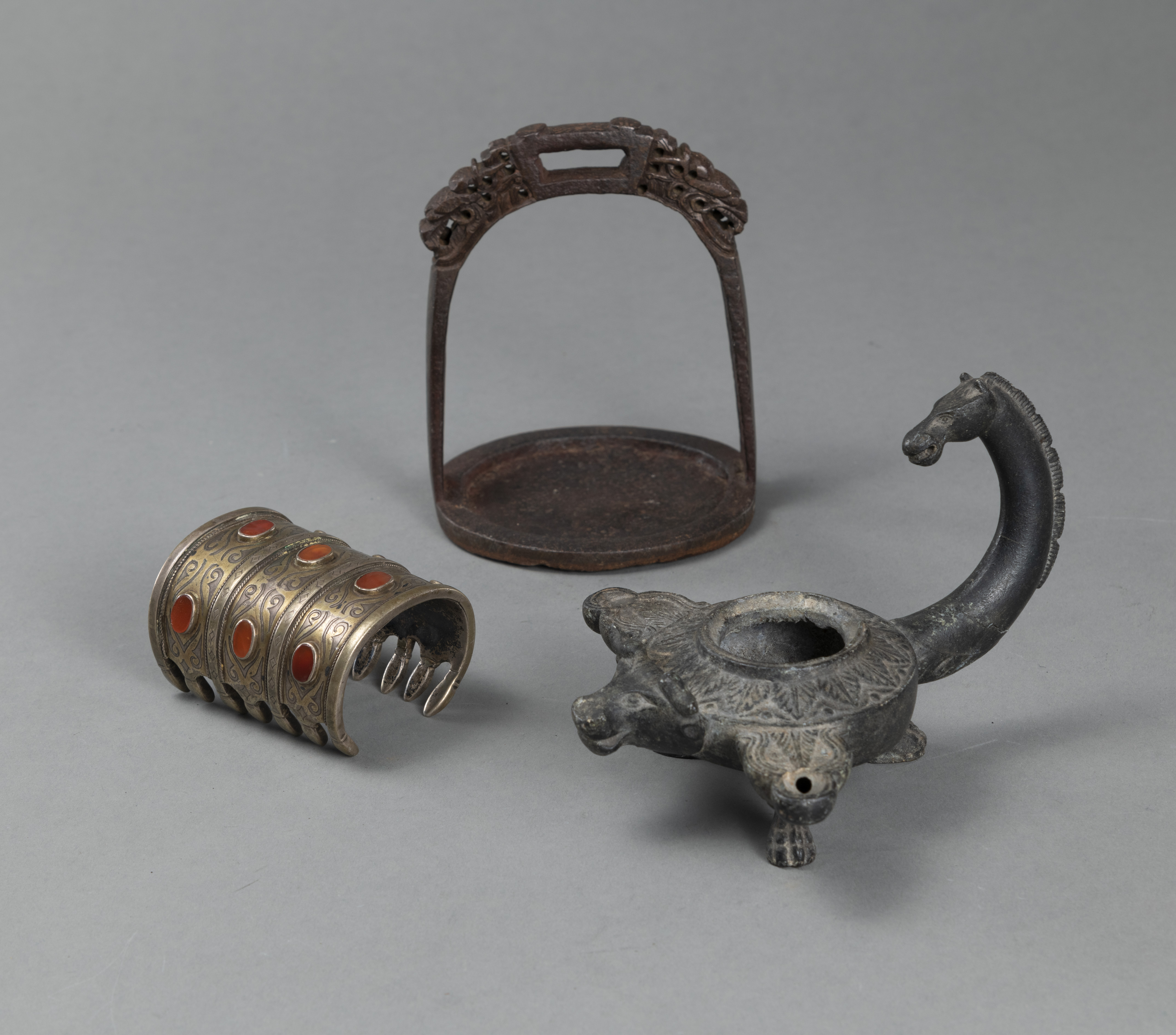AN IRON STIRRUP, A BRACELET WITH CARNELIAN STONES AND A BRONZE OIL LAMP