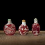 Drei Snuffbottles aus Pekingglas mit rotem Überfangdekor von Wilfgänsen, chilong, Phönix und Melone