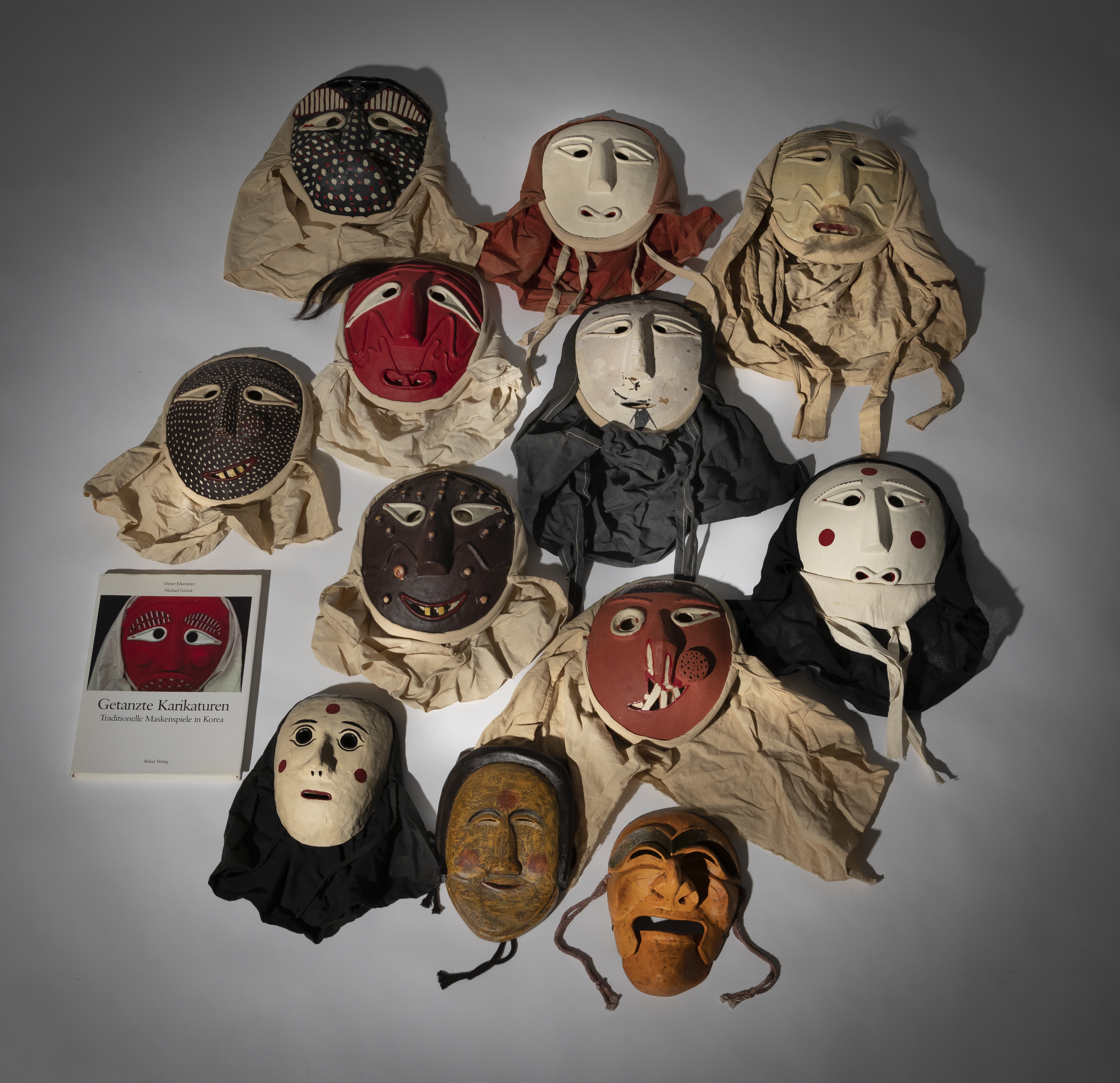 A GROUP OF TWELVE TRADITIOINAL MASKS AND THE BOOK "DANCED CARICATURES" BY DIETER EIKEMEIER