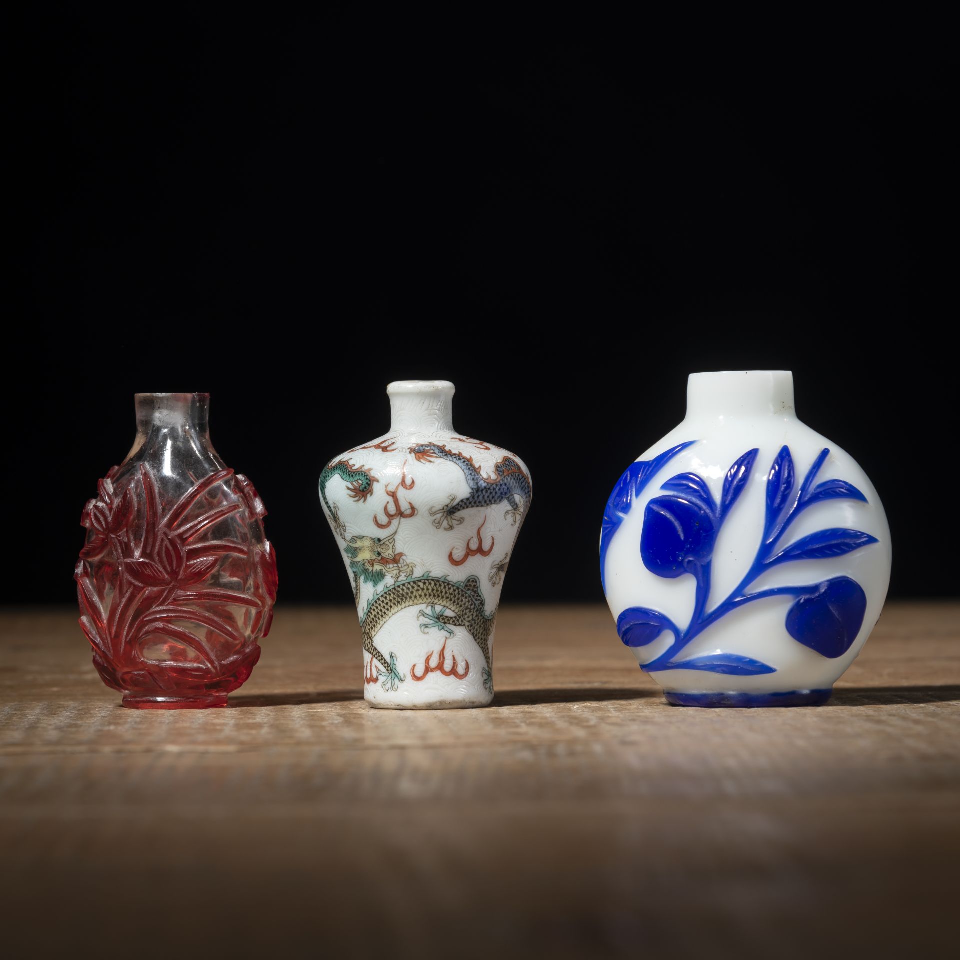 TWO RED- AND BLUE-OVERLAY BEIJING GLASS AND A POLYCHROME DRAGON PORCELAIN SNUFFBOTTLE