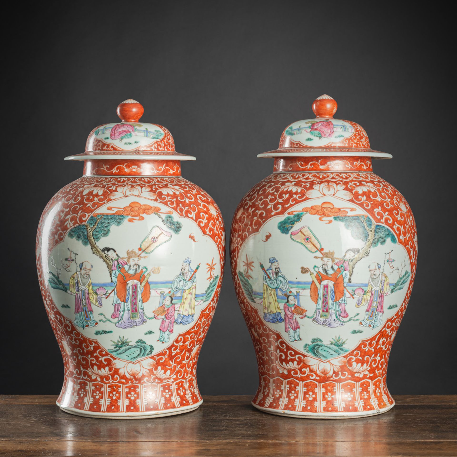 A PAIR OF IRON-RED-GROUND 'FAMILLE ROSE' FIGURAL RESERVES PORCELAIN VASES AND COVERS