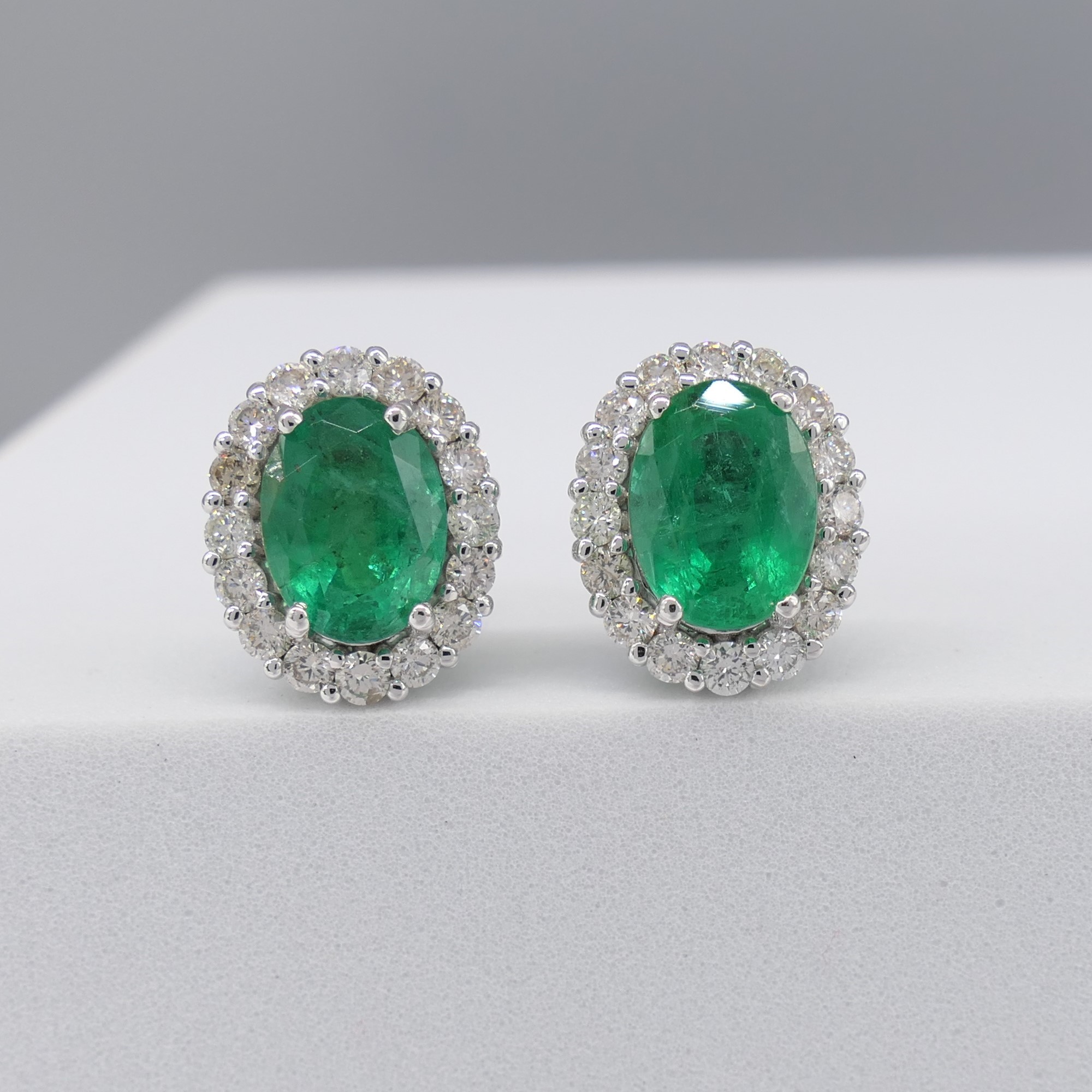 Pair of 18ct white gold oval emerald and diamond cluster ear studs, boxed