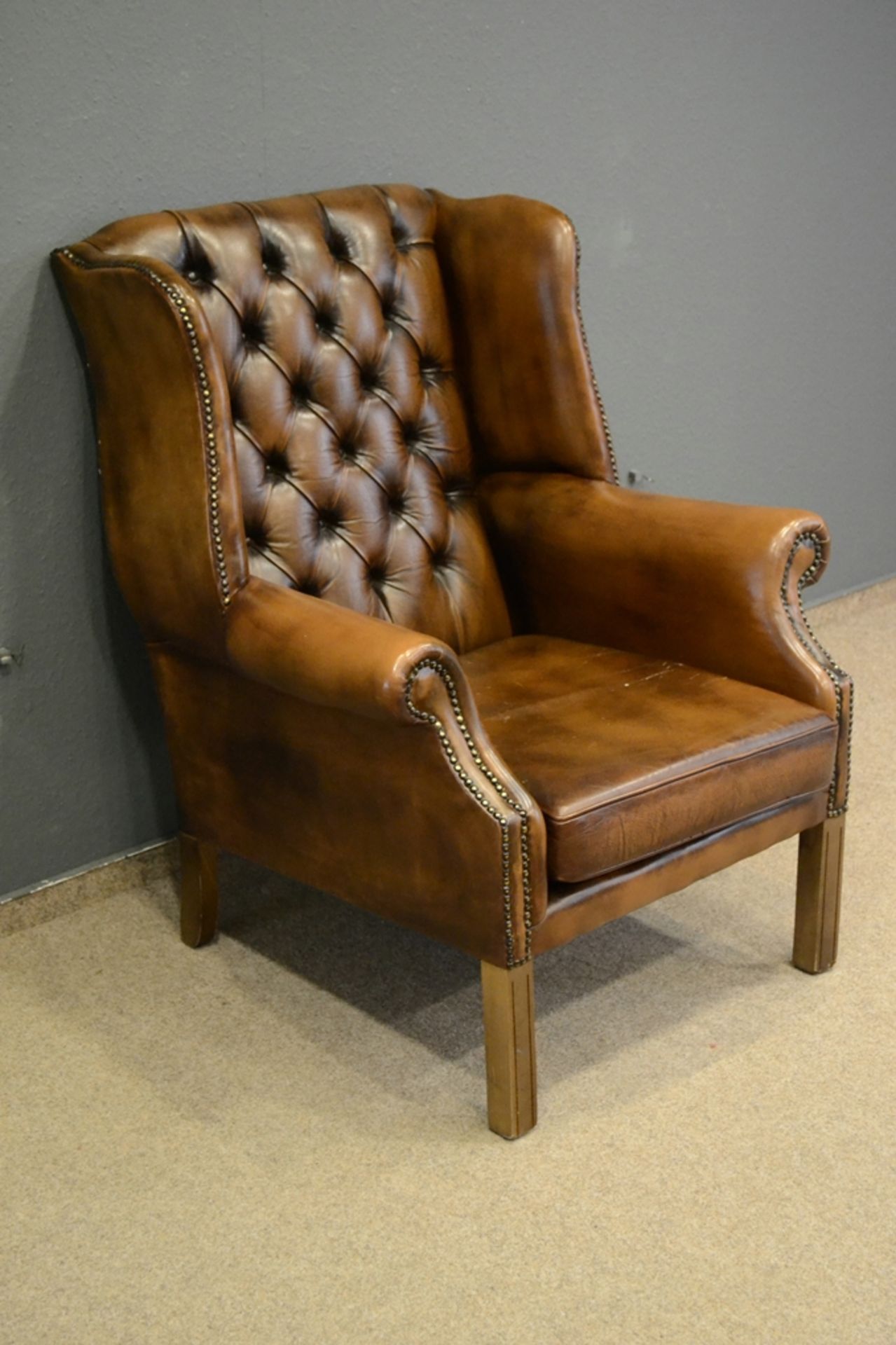 Stilvoller Ohrenbacken-Sessel, bräunliches Leder, leicht eingerollte Armlehnen, der Rücken mit soge