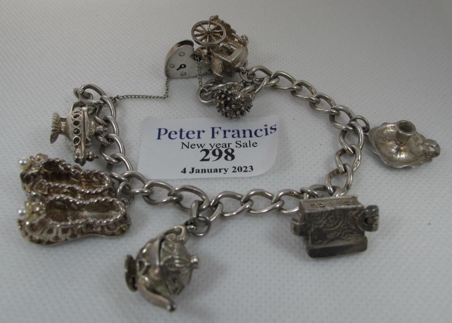 A silver charm bracelet with various charms including a hedgehog, lamp, pair of slippers etc. (B.