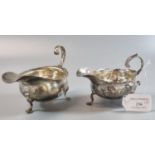 Two silver helmet shaped sauce boats, one standing on hoof feet, the other with repoussé floral