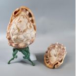 Two carved cameo shells, one on stand, one depicting portrait of a woman the other with cherubs. (2)