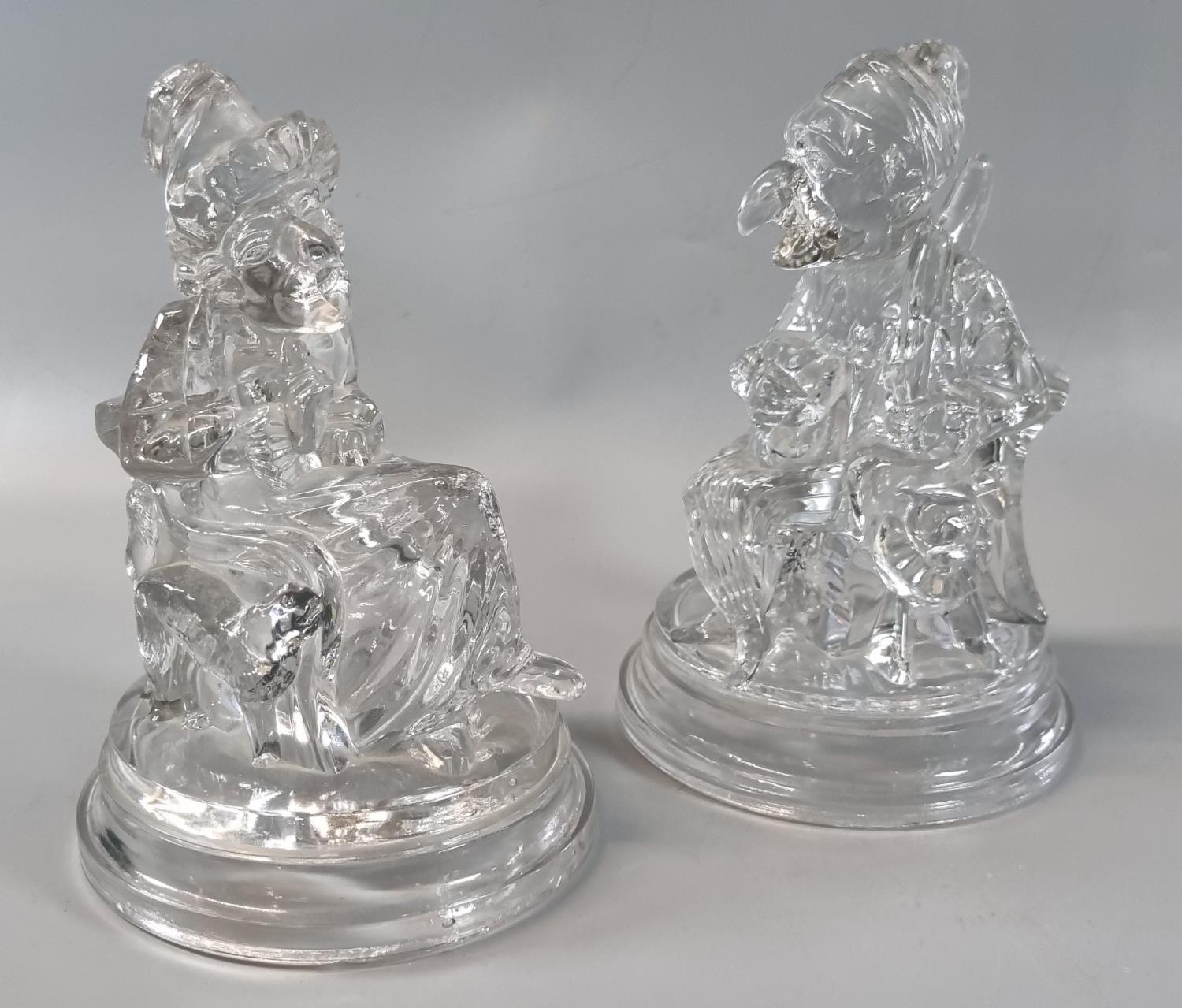 Pair of hollow clear moulded glass figures: 'Punch and Judy', on circular step bases with moulded