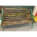 Weathered and slatted garden bench with green painted cast metal scroll decorated bench ends. (B.