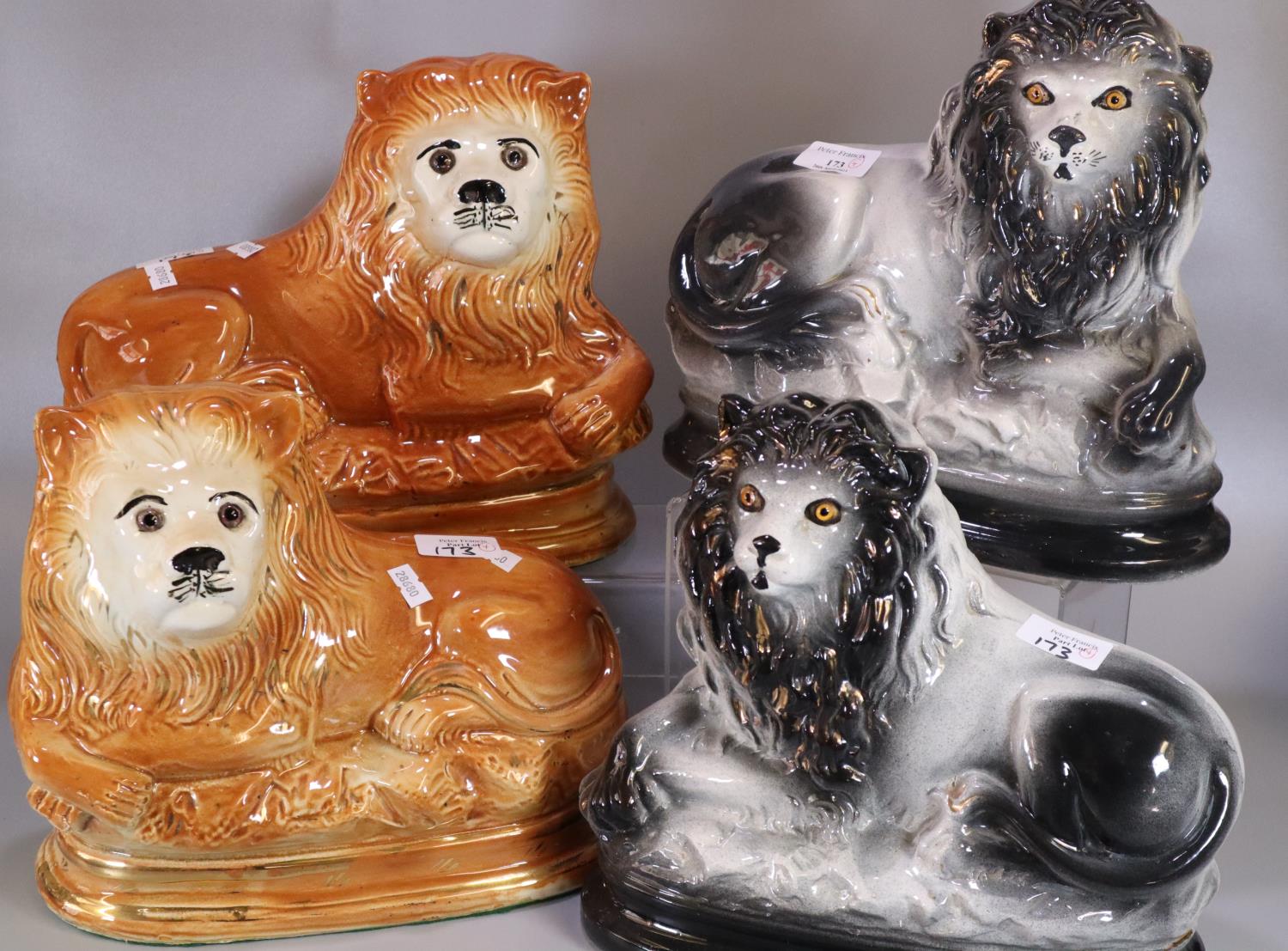 A pair of early 20th Century Staffordshire pottery recumbent male lions with glass eyes, together