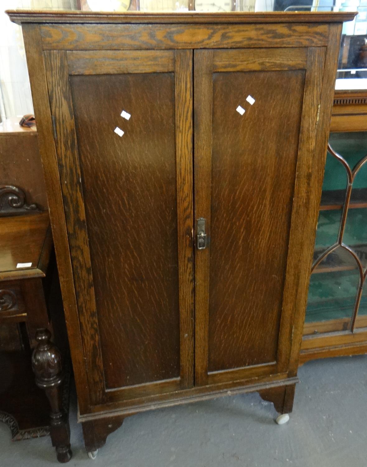 Early 20th century oak two door blind panelled cabinet on wheels, the interior revealing three