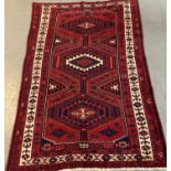 Red ground Persian Hamadan carpet with three lozenge medallions flanked by stylised flowers and