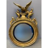 19th century gilt framed convex mirror with carved eagle pediment, moulded foliage and ebonised