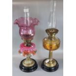 Two early 20th century double burner oil lamps, one with cranberry coloured shade, clear chimney and