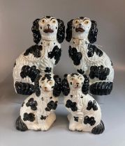 Two pairs of black and white Staffordshire pottery seated fireside spaniels of different sizes. (B.