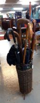 Modern wicker work and metal umbrella stand with a collection of walking sticks, umbrellas,
