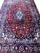 Red and blue ground Persian Kashan carpet with traditional floral designs. 285x176cm approx. (B.P.