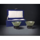 A MOTTLED PAIR OF CHINESE SPINACH JADE BOWLS. MID 20TH CENTURY. IN ORIGINAL BOX, WITH WOODEN STANDS.