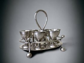 A DR CHRISTOPHER DRESSER DESIGN EGG CRUET SET, BY HUKIN & HEATH. SIX EGG CUPS WITH LOOPED HANDLE.