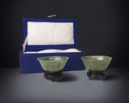 A MOTTLED PAIR OF CHINESE SPINACH JADE BOWLS. MID 20TH CENTURY. IN ORIGINAL BOX, WITH WOODEN STANDS.