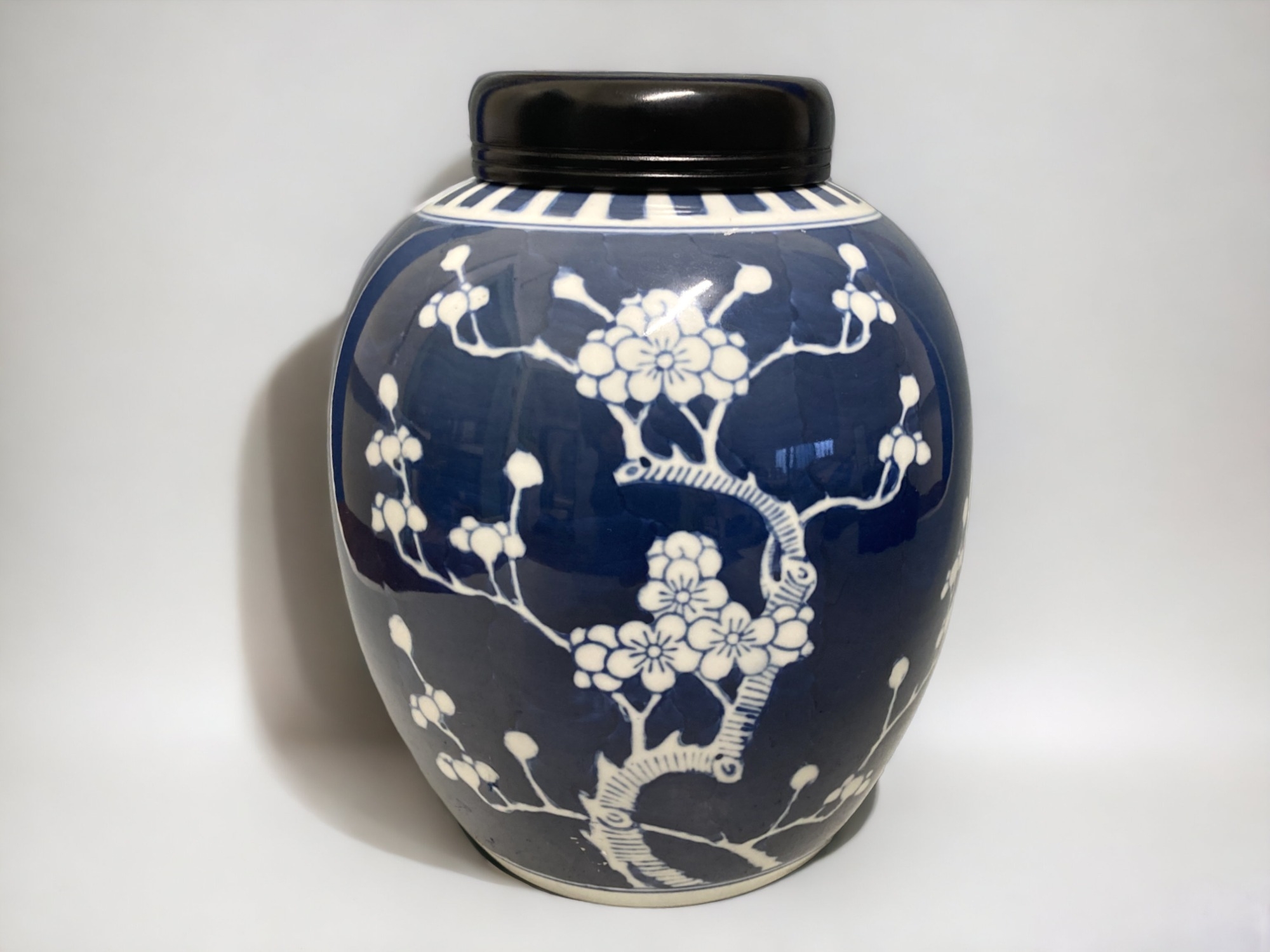 A LARGE CHINESE PORCELAIN JAR & WOODEN COVER. PAINTED PRUNUS PATTERN. HEIGHT - 25CM