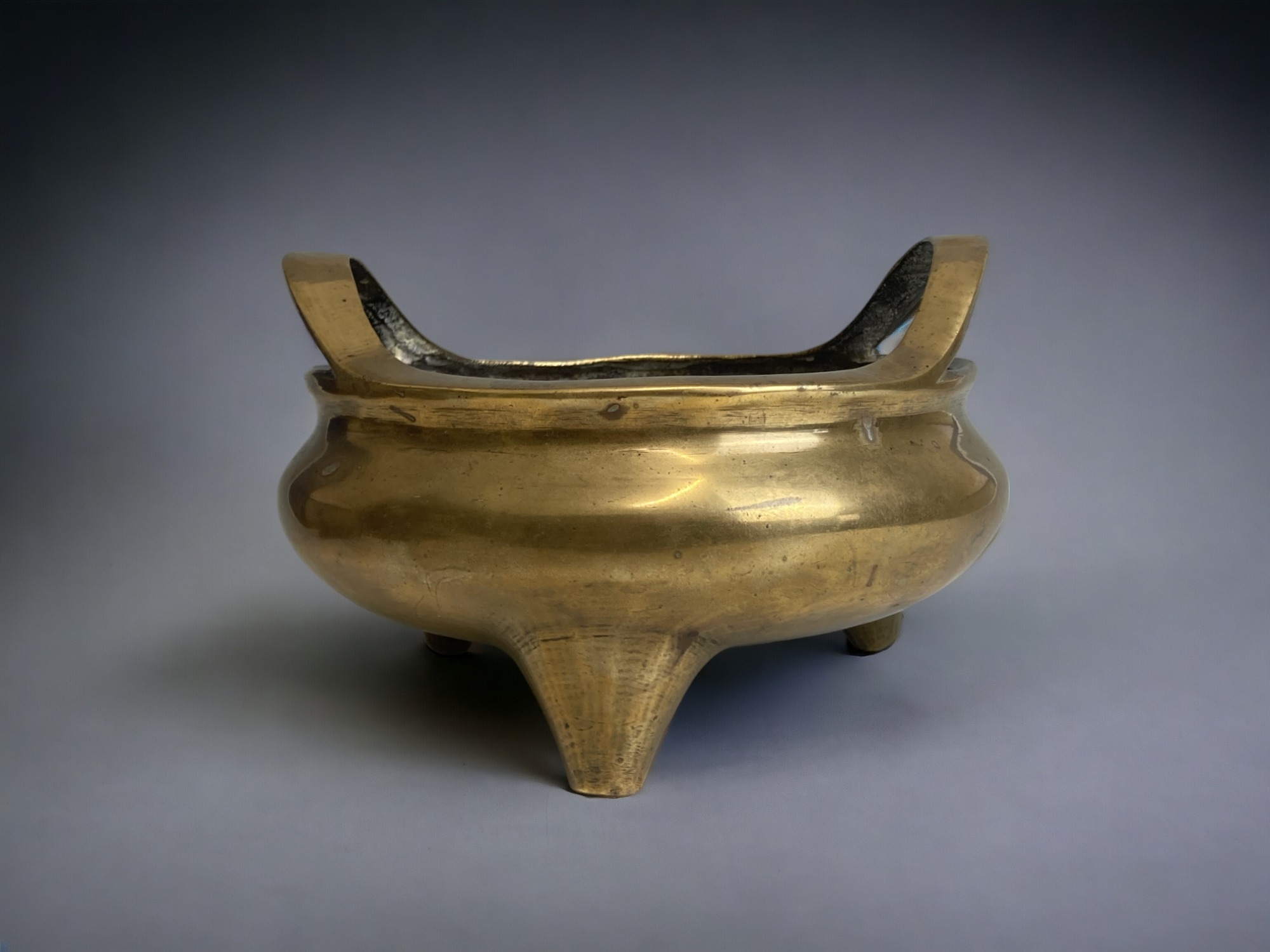 A large Chinese polished bronze twin handle censer. Qing dynasty. Raised on three tapered feet.