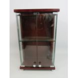 A small table top glass fronted cabinet, 14" tall, 8.5" wide and 5" deep.