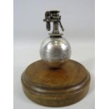 White metal cricket ball table lighter standing on a wooden base.