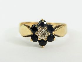 9ct Yellow Gold ring set with a small Central Diamond and surrounded by six small Sapphires. .. Fin