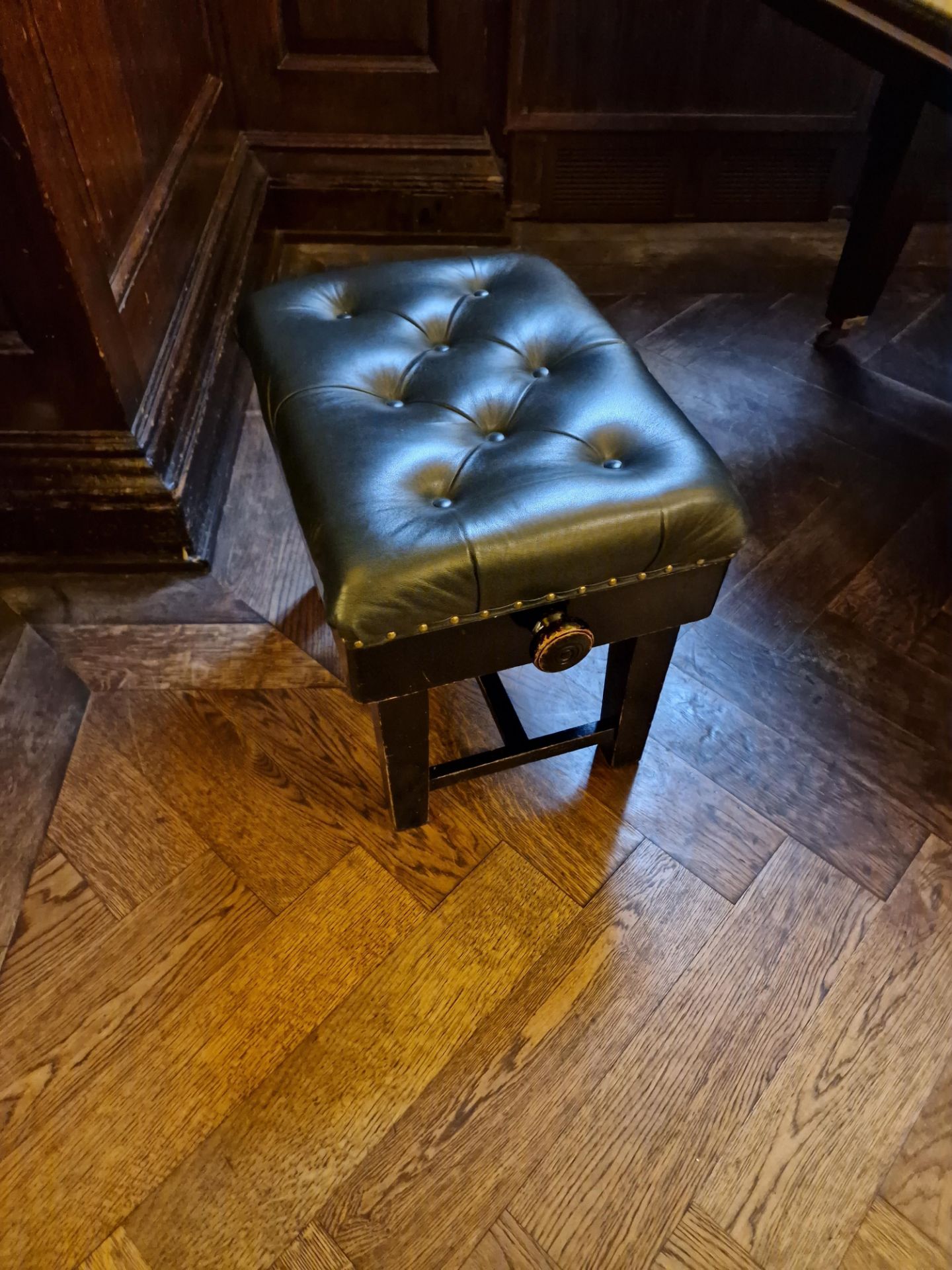 A tufted green leather piano stool with stud pin detail on a mahogany timber frame height adjustable