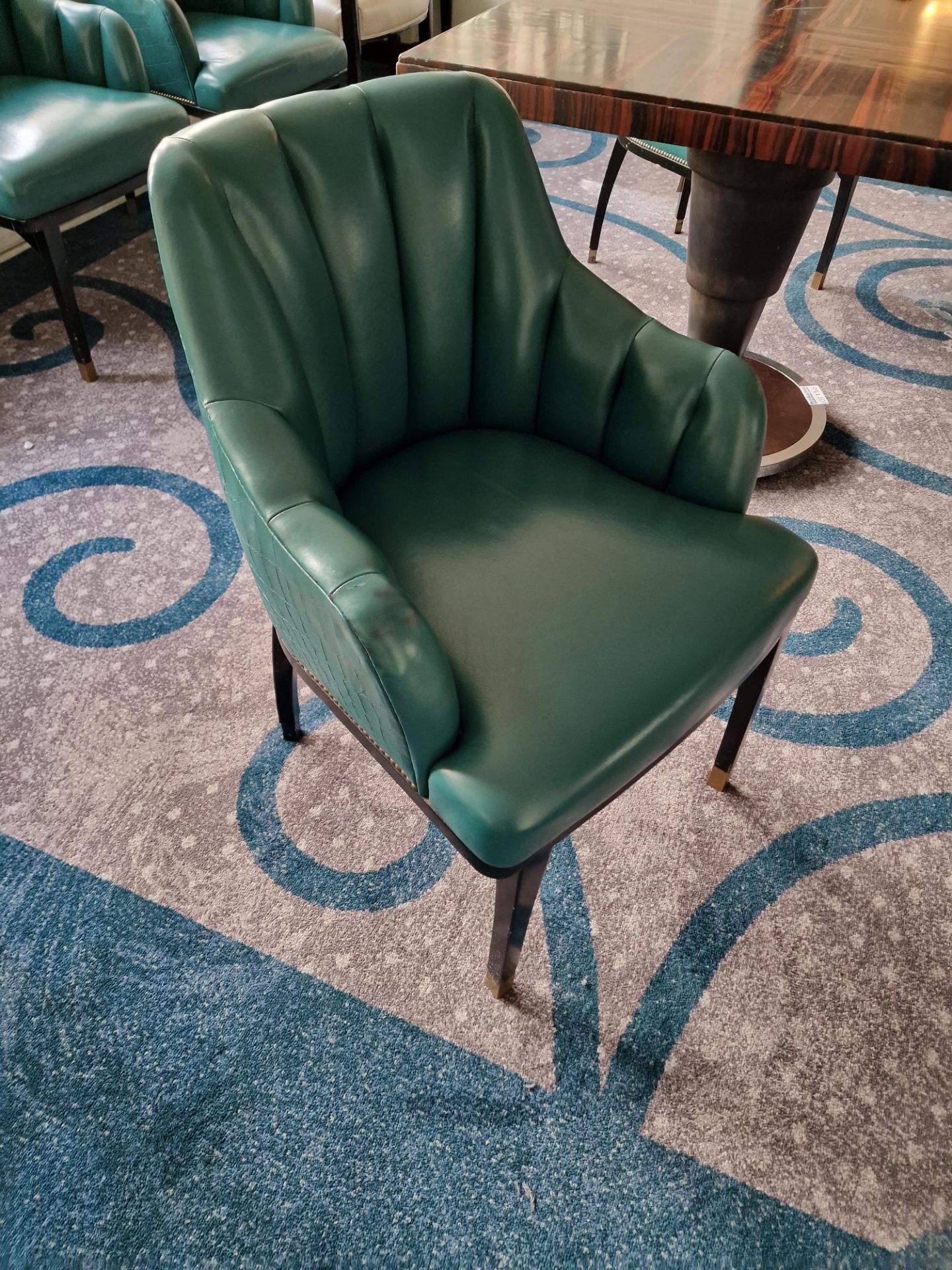 A pair of armchairs upholstered in green leather with a stud pin detailing the arm partially