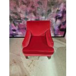 A contemporary red velvet upholstered low level arm chair with short sloped arm rests and padded