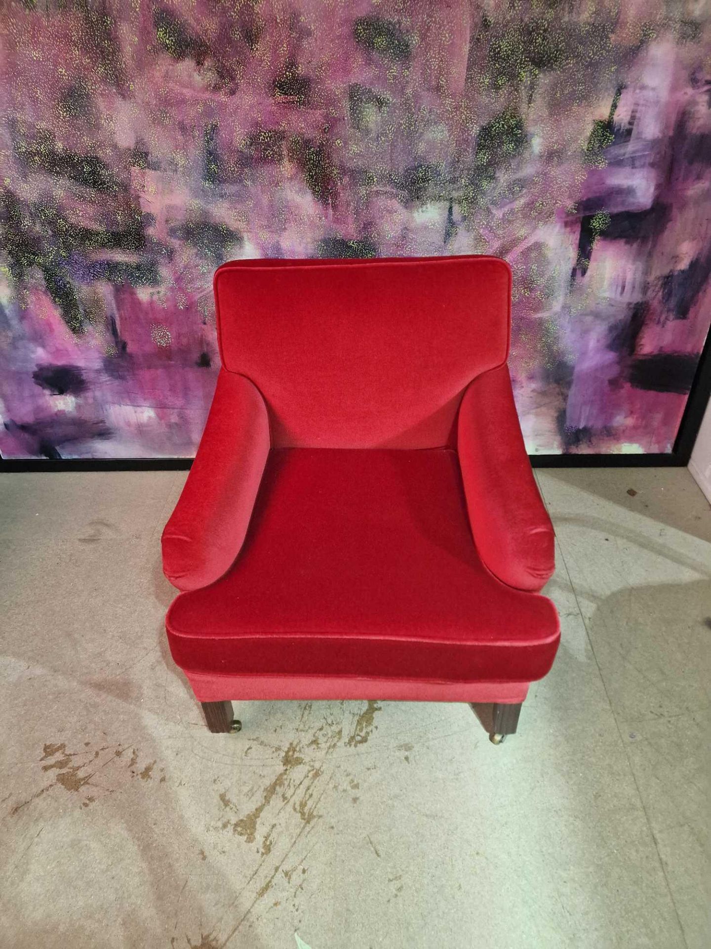 A contemporary red velvet upholstered low level arm chair with short sloped arm rests and padded