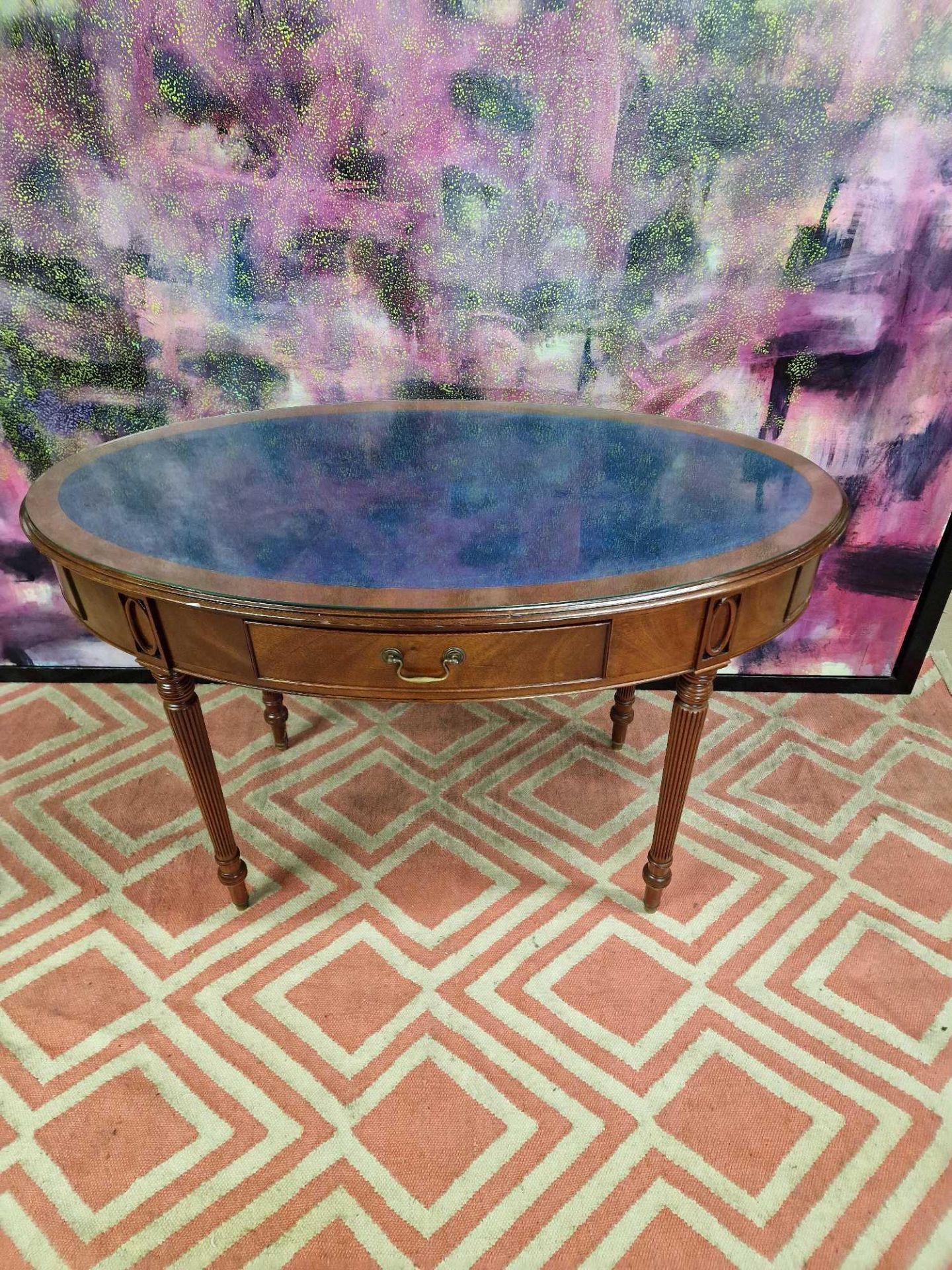Oval writing table with blue tooled leather inlay under a protective glass top, the apron features
