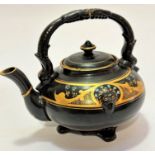 A pottery black glazed and gilded teapot with lion mask moulding to border with Forget Me Nots to