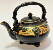 A pottery black glazed and gilded teapot with lion mask moulding to border with Forget Me Nots to