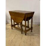 An early 20th century oak drop leaf table, the oval top on turned and block supports with gate leg
