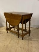 An early 20th century oak drop leaf table, the oval top on turned and block supports with gate leg