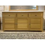 A contemporary light oak sideboard, fitted with three drawers over three panelled doors, raised on