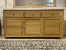 A contemporary light oak sideboard, fitted with three drawers over three panelled doors, raised on