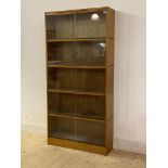 A mid century oak five height stacking bookcase, each section with two glazed sliding doors, stamped