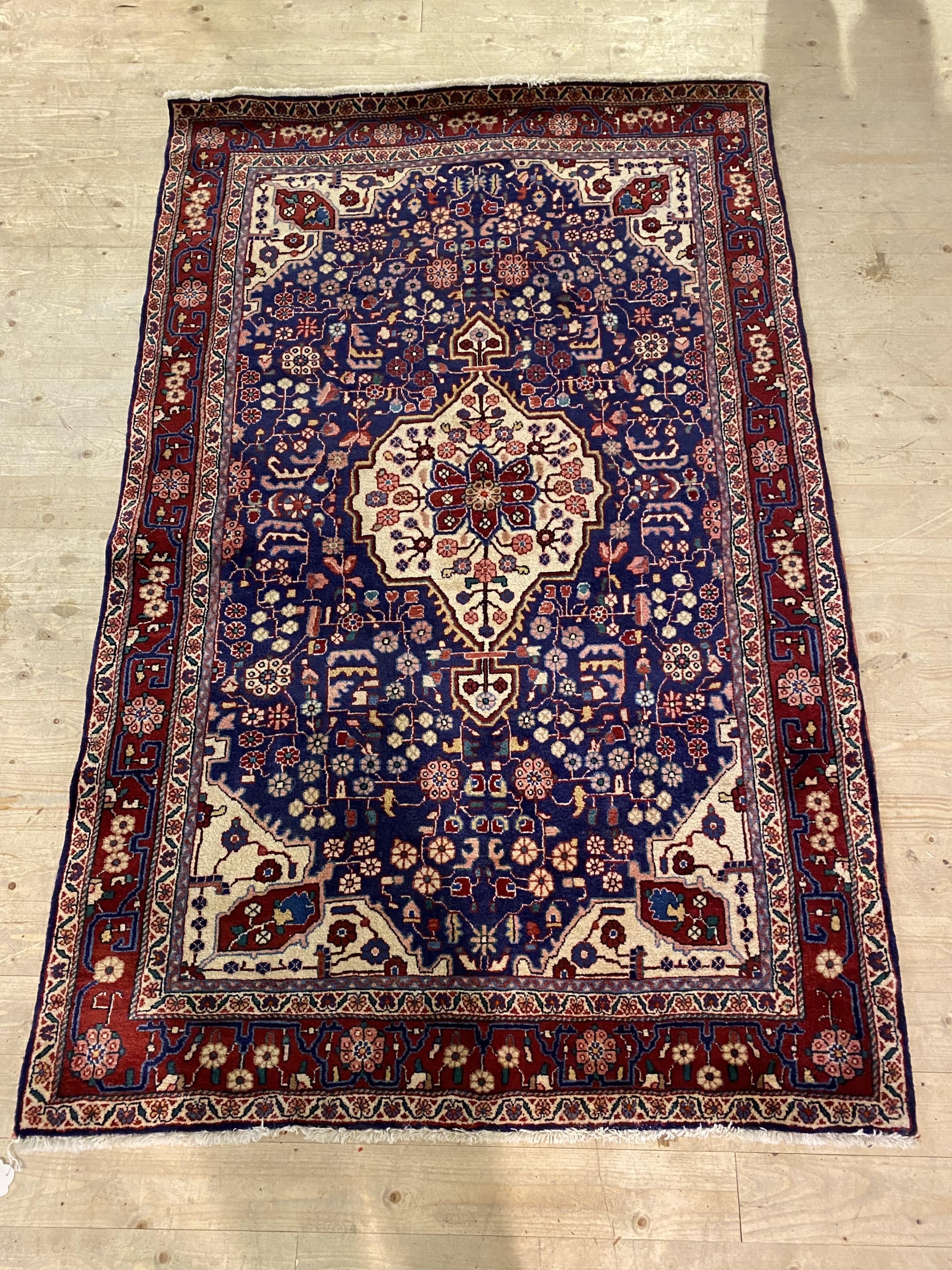 A Persian hand knotted rug, the busy blue field centred by an ivory medallion and bordered 133cm x