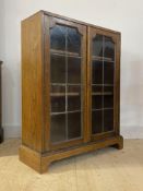 A 1930's oak bookcase, with twin lead glazed doors enclosing two adjustable shelves, raised on