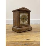 An Edwardian oak cased mantle time piece clock, the domed top over floral scroll carved frieze and