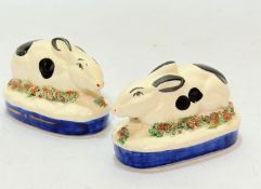 A pair of Staffordshire style seated rabbit pottery figures raised on oval floral mounted bases